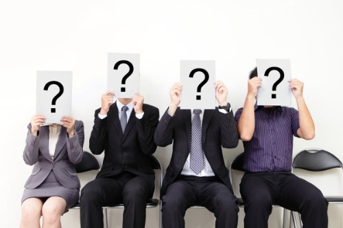 Stand out at interviews, photo of people waiting to be interviewed holding a sign with a question mark in front of their face